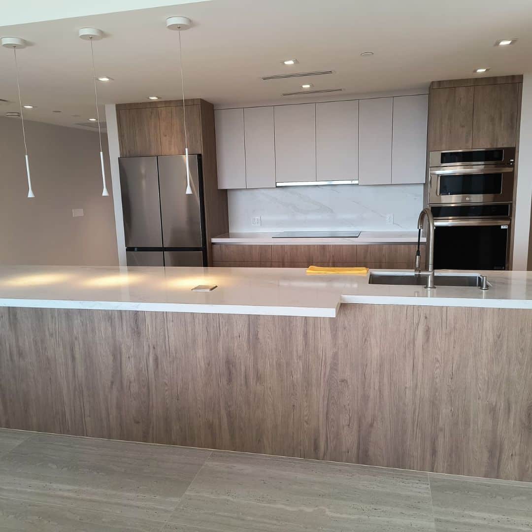 Modern minimalist kitchen with a large island, light wood veneer cabinets, and gray upper cabinetry.