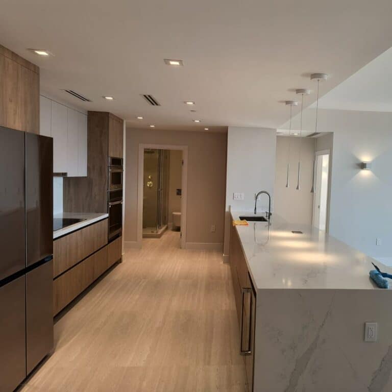 Open-plan modern kitchen featuring light wood and white cabinetry, a large white quartz island, and a view into a bathroom with a glass shower.