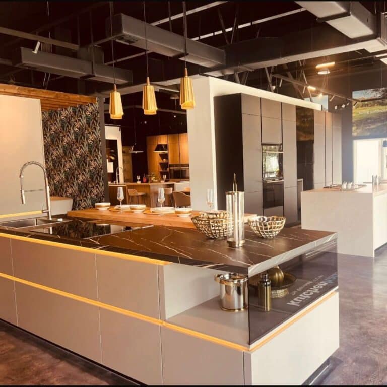 High-end kitchen showroom display featuring a dark marble island with integrated lighting, sleek gray cabinetry, and gold pendant lamps.