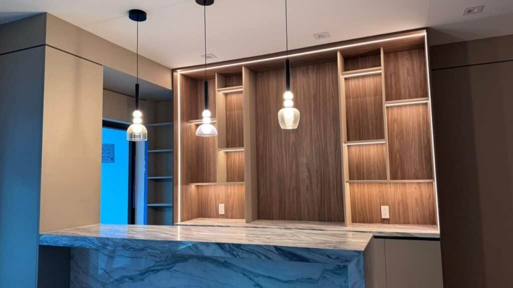 Luxury home bar with marble waterfall countertop, custom wood shelving, and elegant pendant lighting.