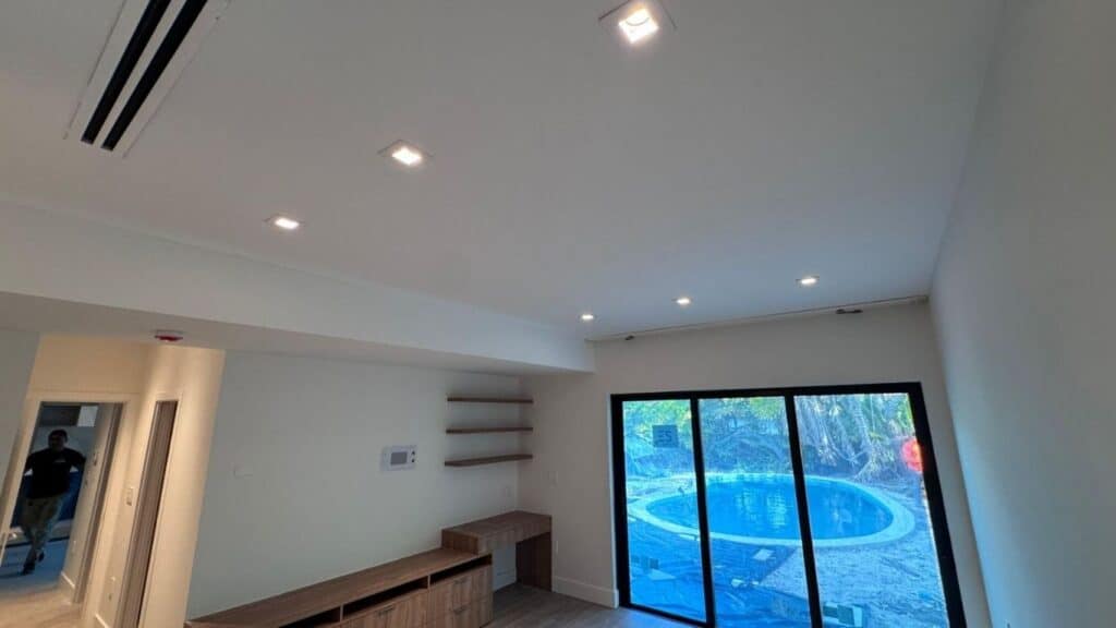 Modern living room with recessed square LED ceiling lights, minimalist wood floating desk, and large sliding glass doors.