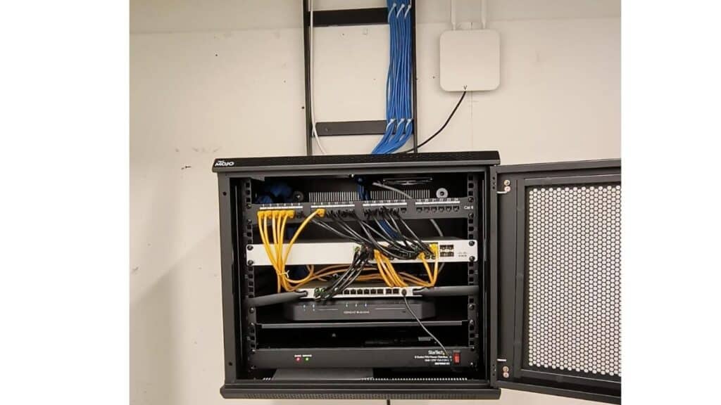 Wall-mounted network rack with patch panels, Ethernet switches, and organized cable management.
