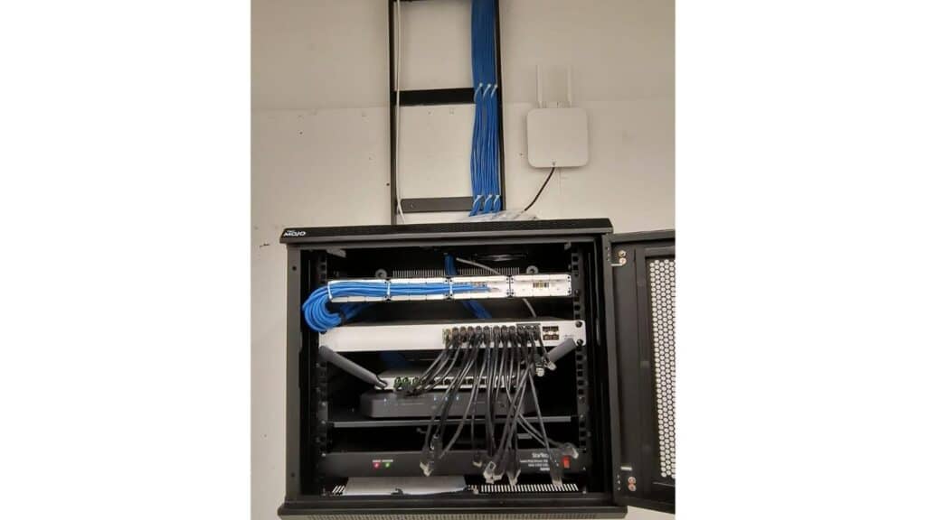 Wall-mounted IT network rack with structured blue Ethernet cabling, patch panels, and network switches.