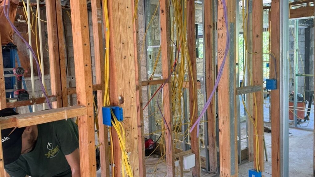 Electrical rough-in with yellow Romex wiring and blue junction boxes in a wood frame structure.