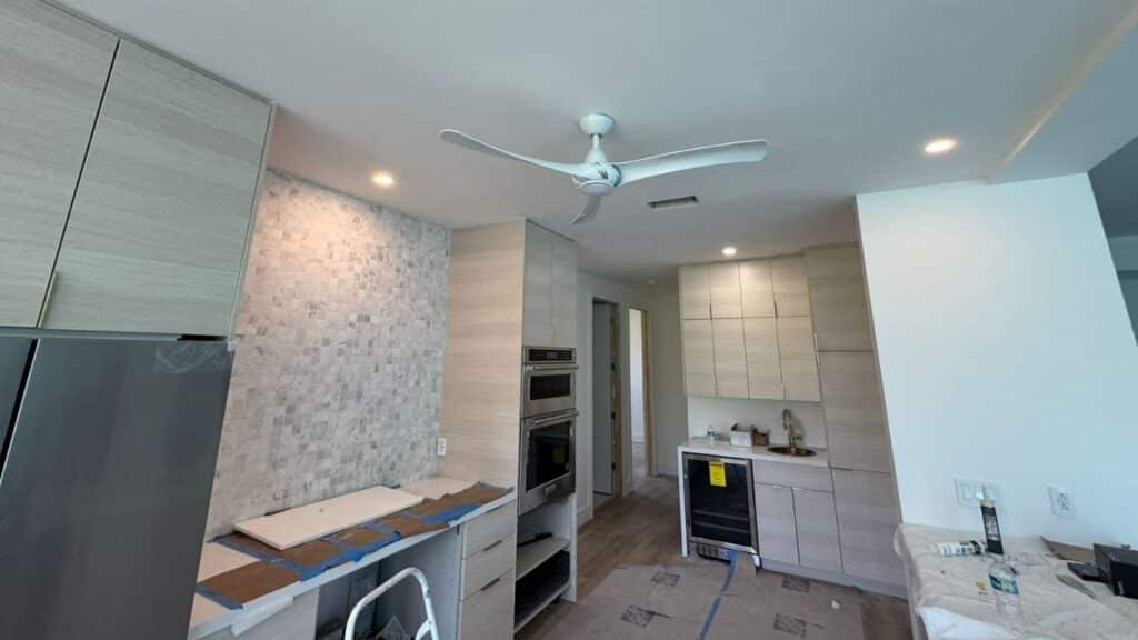 Modern kitchen remodel with light wood cabinetry, mosaic tile backsplash, and white ceiling fan.