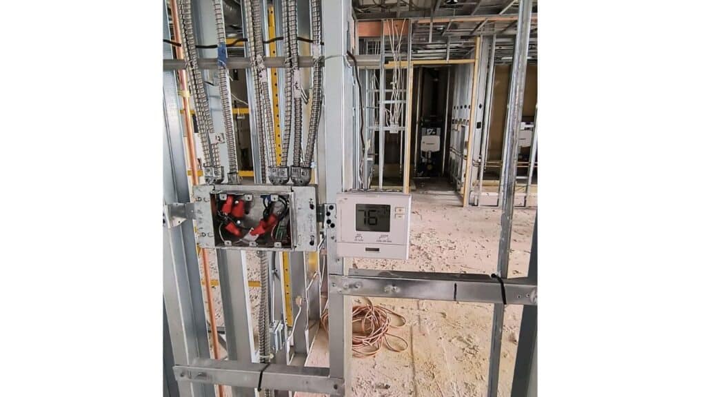 HVAC thermostat installation and armored cable wiring in a commercial metal stud frame.