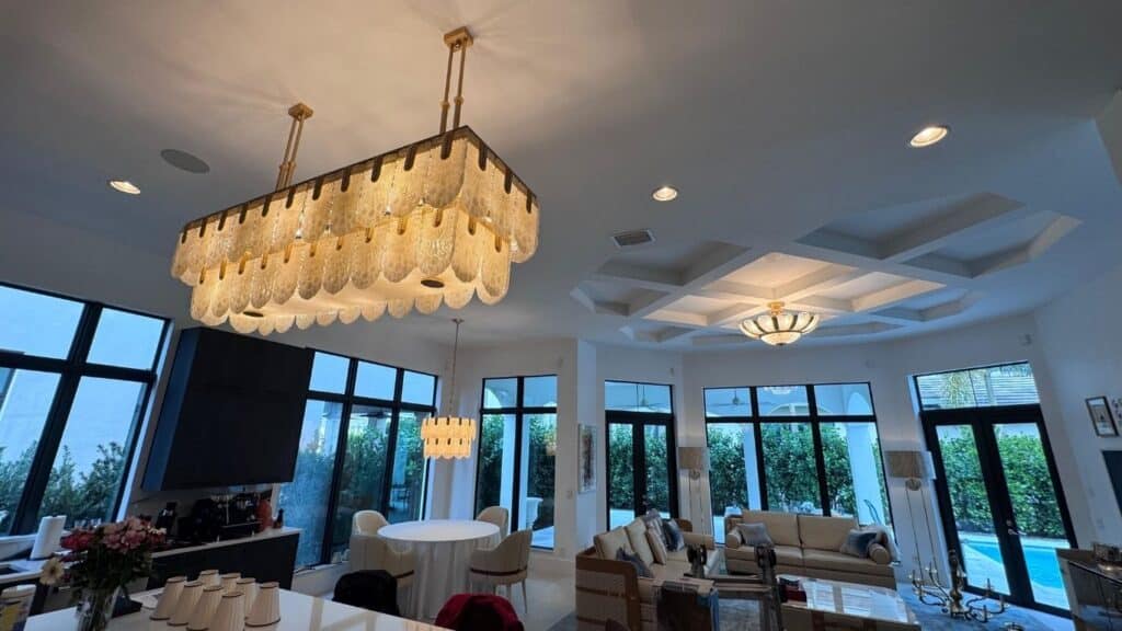 Luxury open-concept living area featuring a grand tiered glass chandelier and coffered ceiling with integrated lighting.