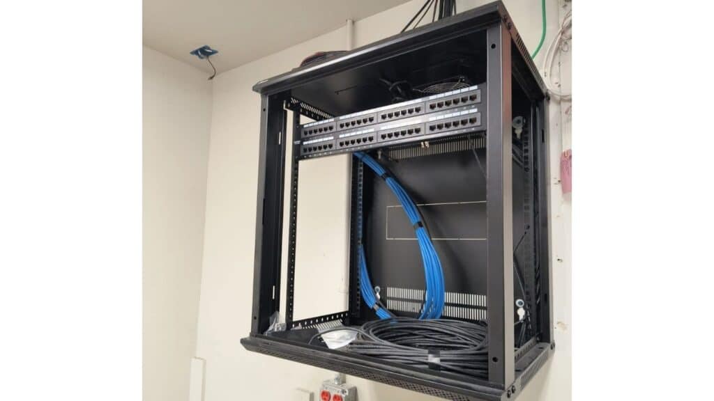Wall-mounted open server rack installation with patch panels and blue Ethernet cabling rough-in.