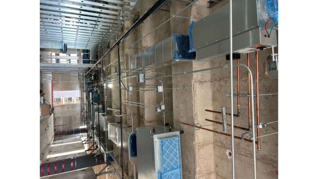 Large-scale commercial HVAC installation featuring galvanized steel ductwork, copper refrigerant lines, and terminal units in a high-ceiling concrete structure.
