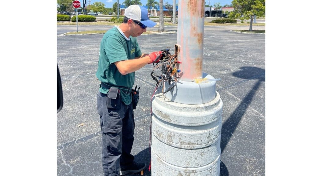 Electrician performing parking lot light repair and wiring maintenance on a commercial light pole base.